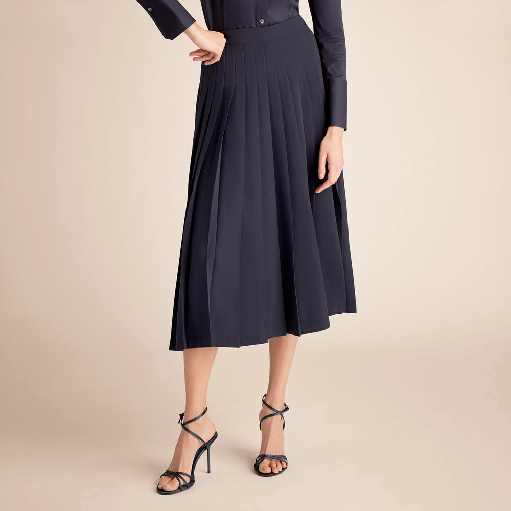 Person wearing a black pleated skirt and black heels on a beige background
