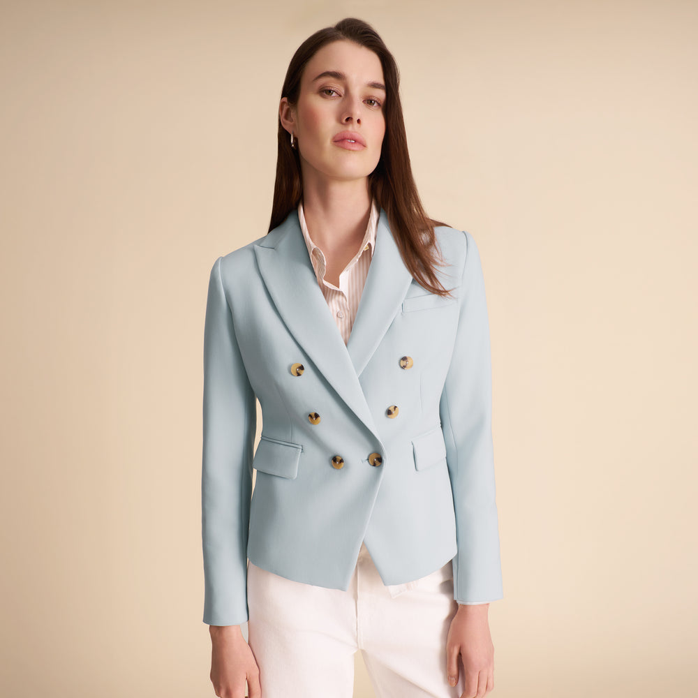 Woman wearing a light blue blazer with gold buttons on a beige background