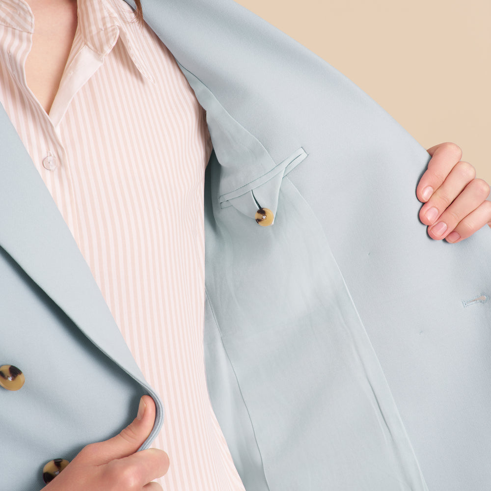 Light blue blazer with a pink shirt underneath, held by hands on a beige background