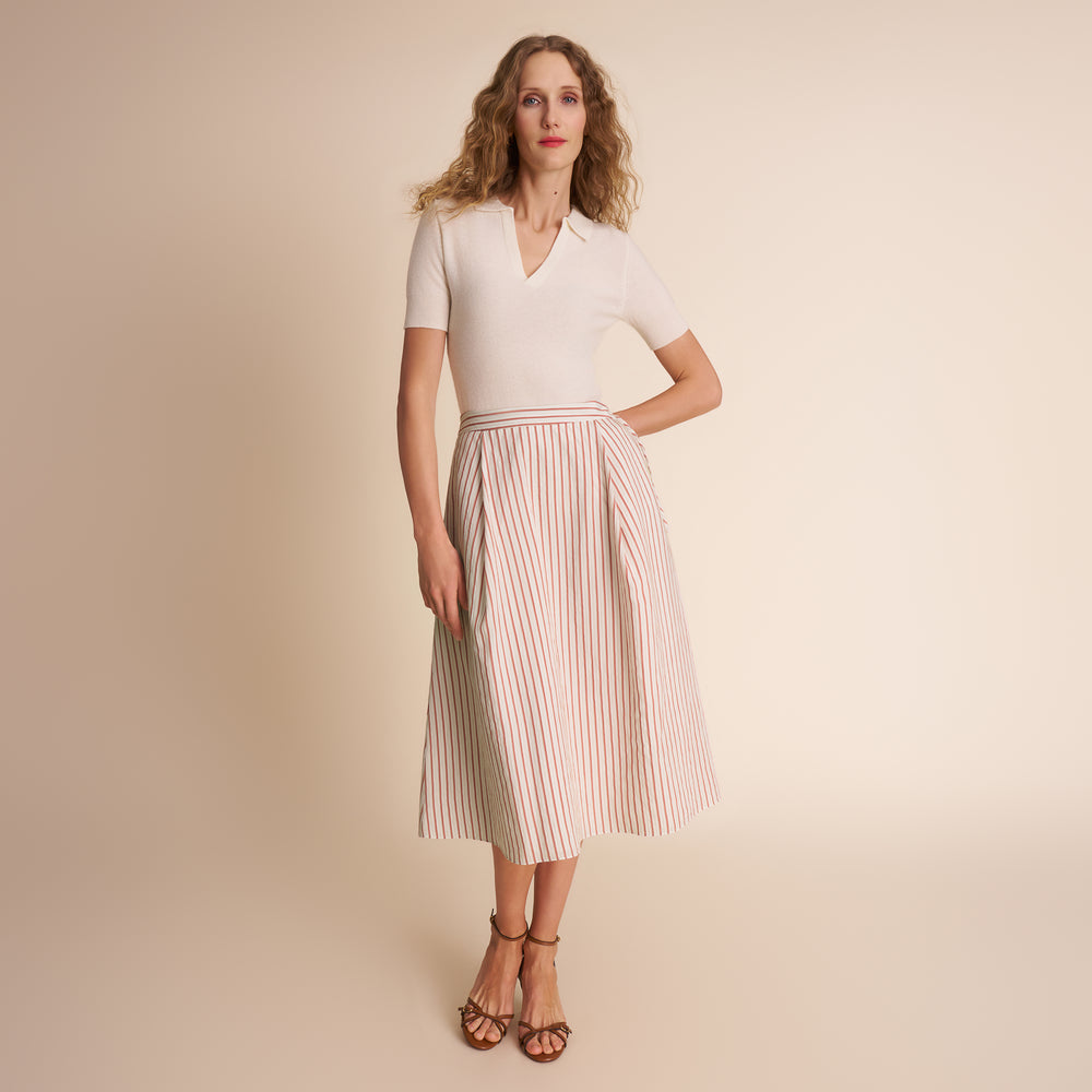 Woman wearing a white top and striped skirt on a beige background