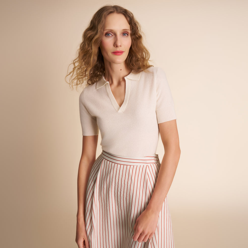 Woman wearing a white polo shirt and striped skirt against a beige background