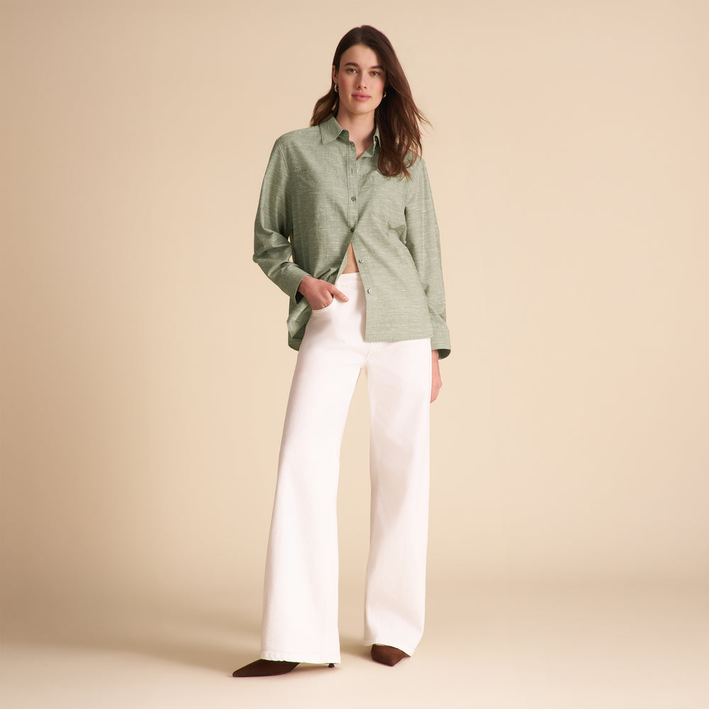 Woman wearing a green shirt and white pants on a beige background