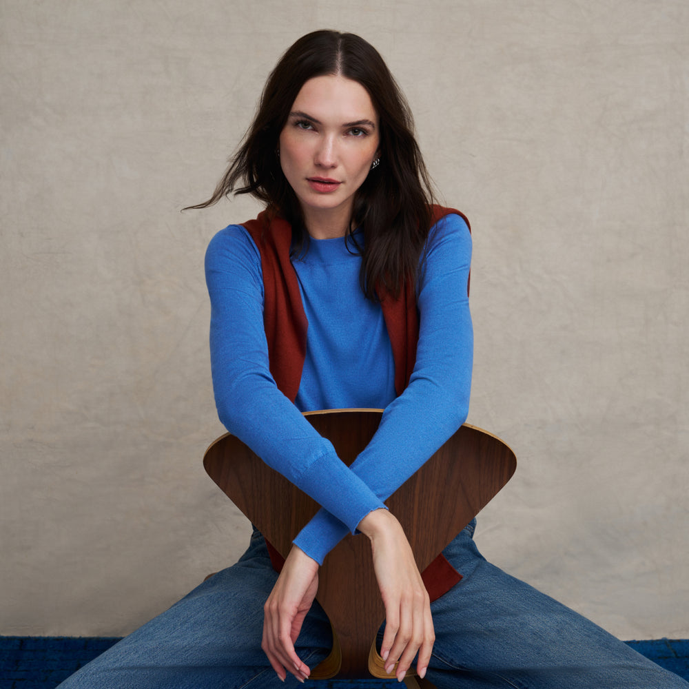 Woman wearing a long sleeve splendor blue sweater and jeans on a blue carpet floor and against a beige background