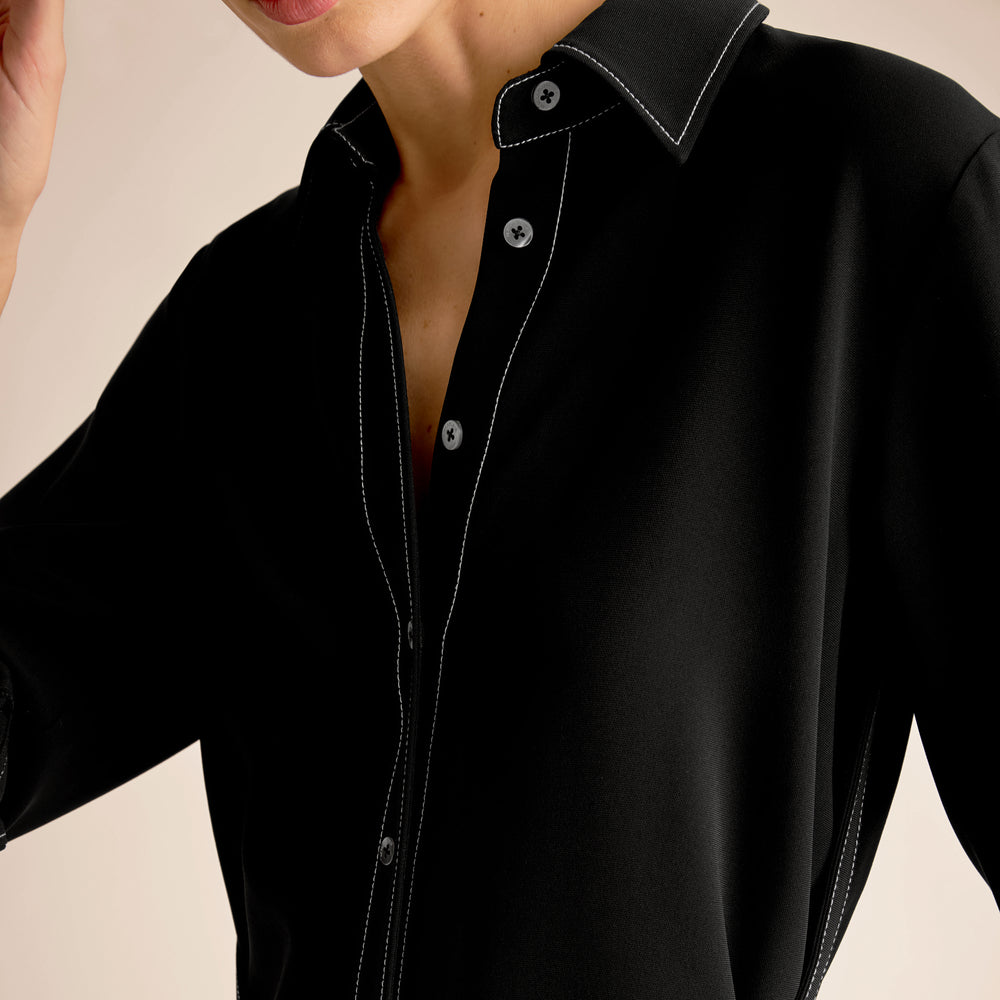 Close-up of a person wearing a black shirt with white buttons on a beige background