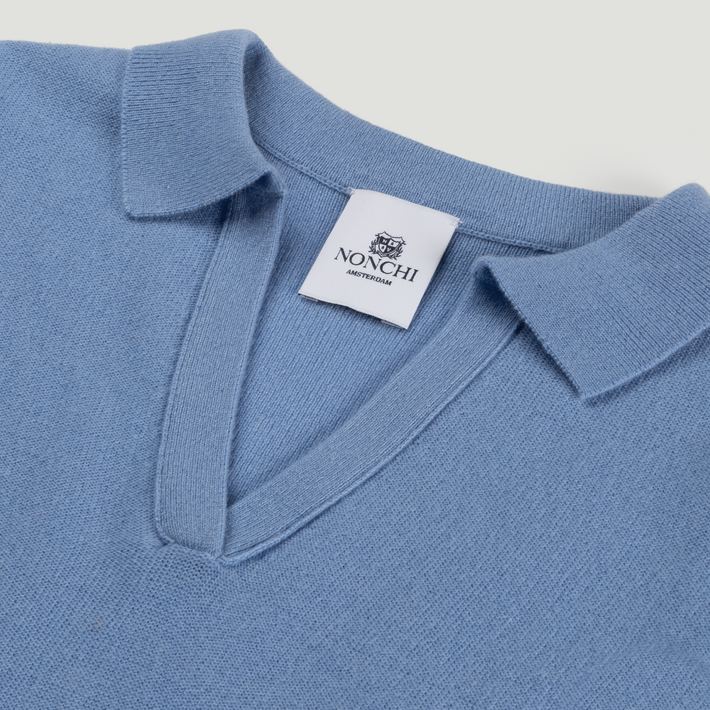 Close-up of a blue polo shirt with a Nonchi label on a light gray background