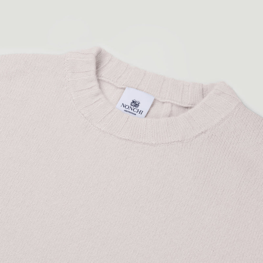 Close-up of a light pink sweater with a brand label on a white background