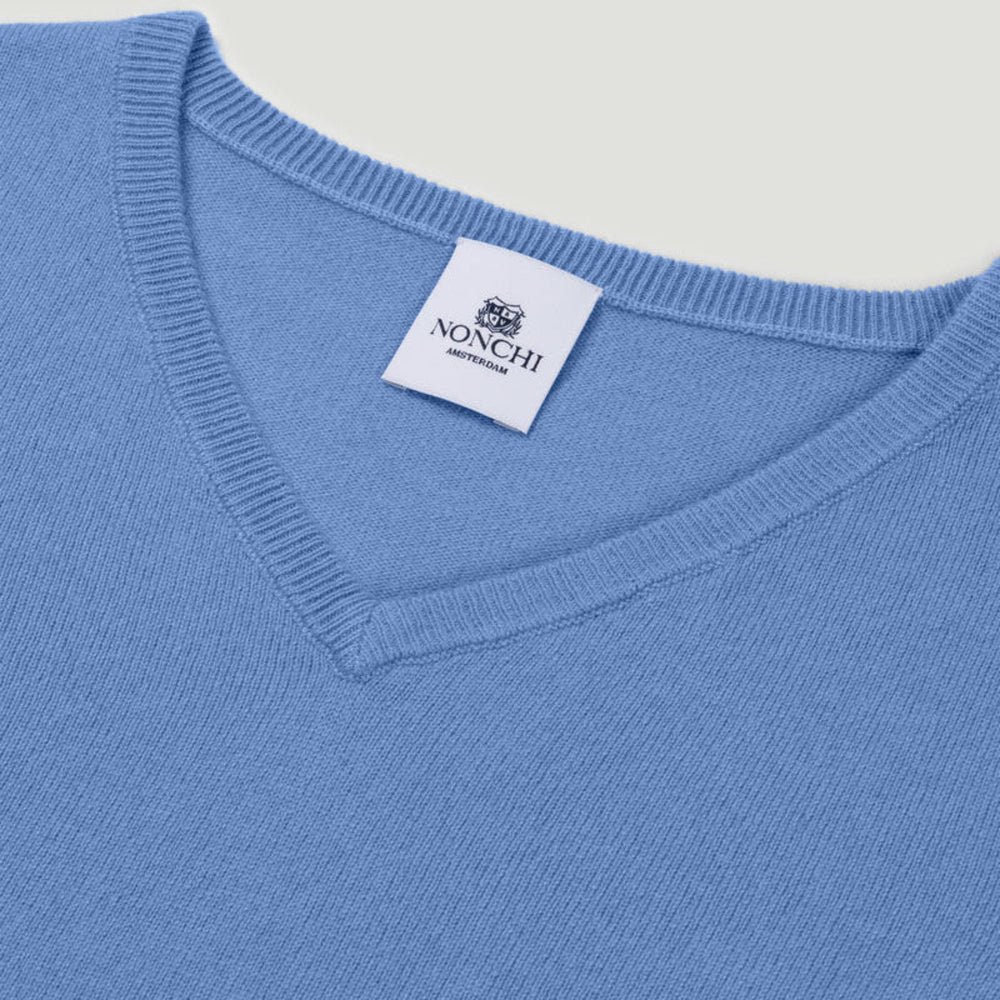 Close-up of a blue sweater with a Nonchi label on a light gray background.