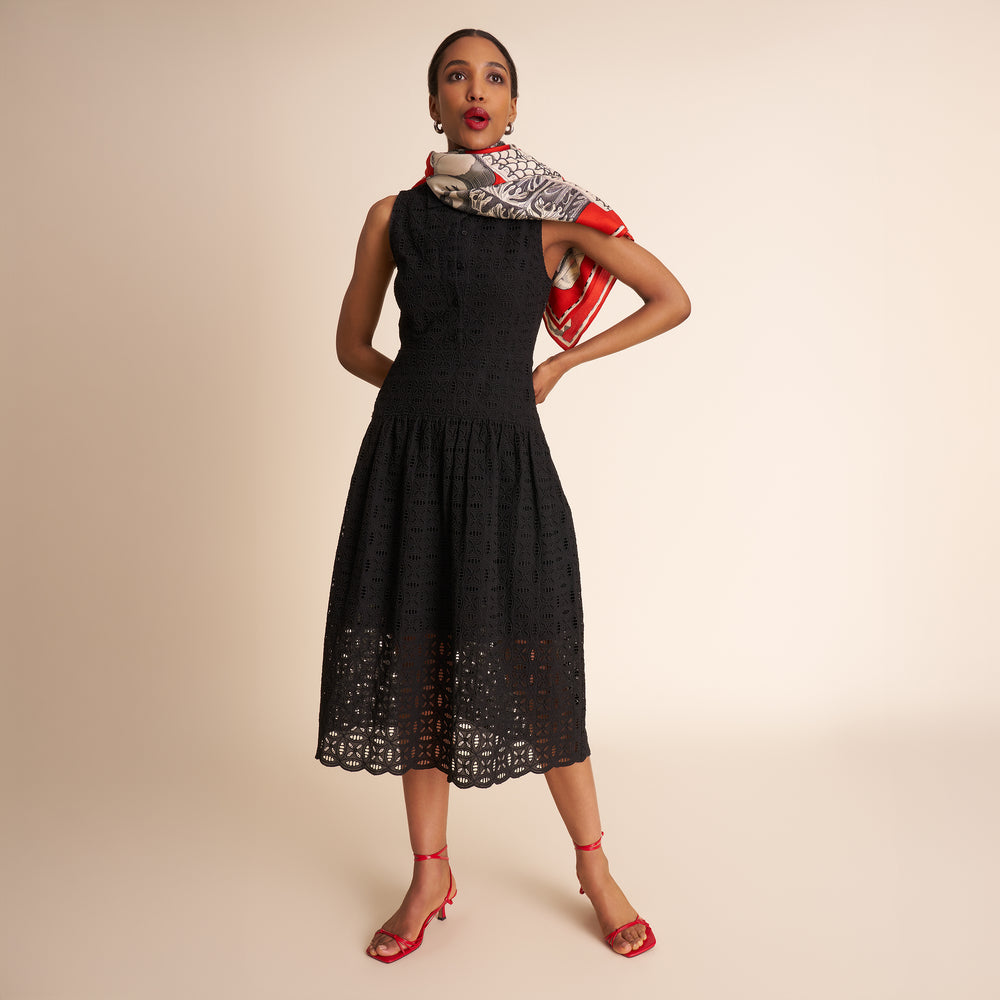 Woman wearing a black dress with lace details and a patterned scarf on a beige background.