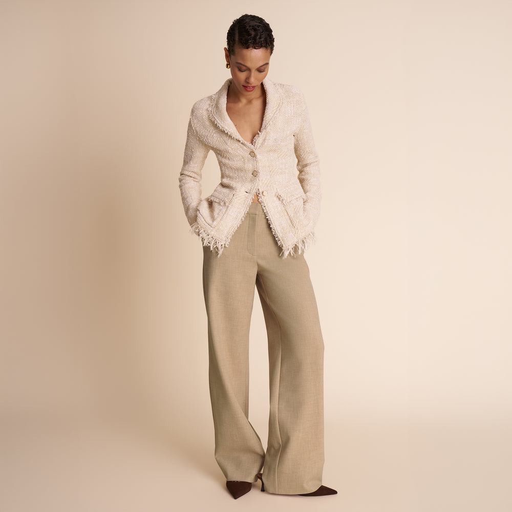 Woman wearing a white lace top and beige pants on a beige background