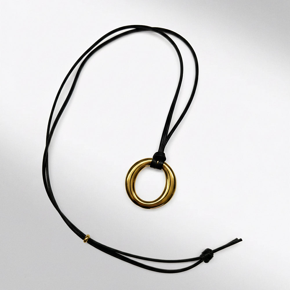 Necklace with a gold ring pendant on a black cord against a white background