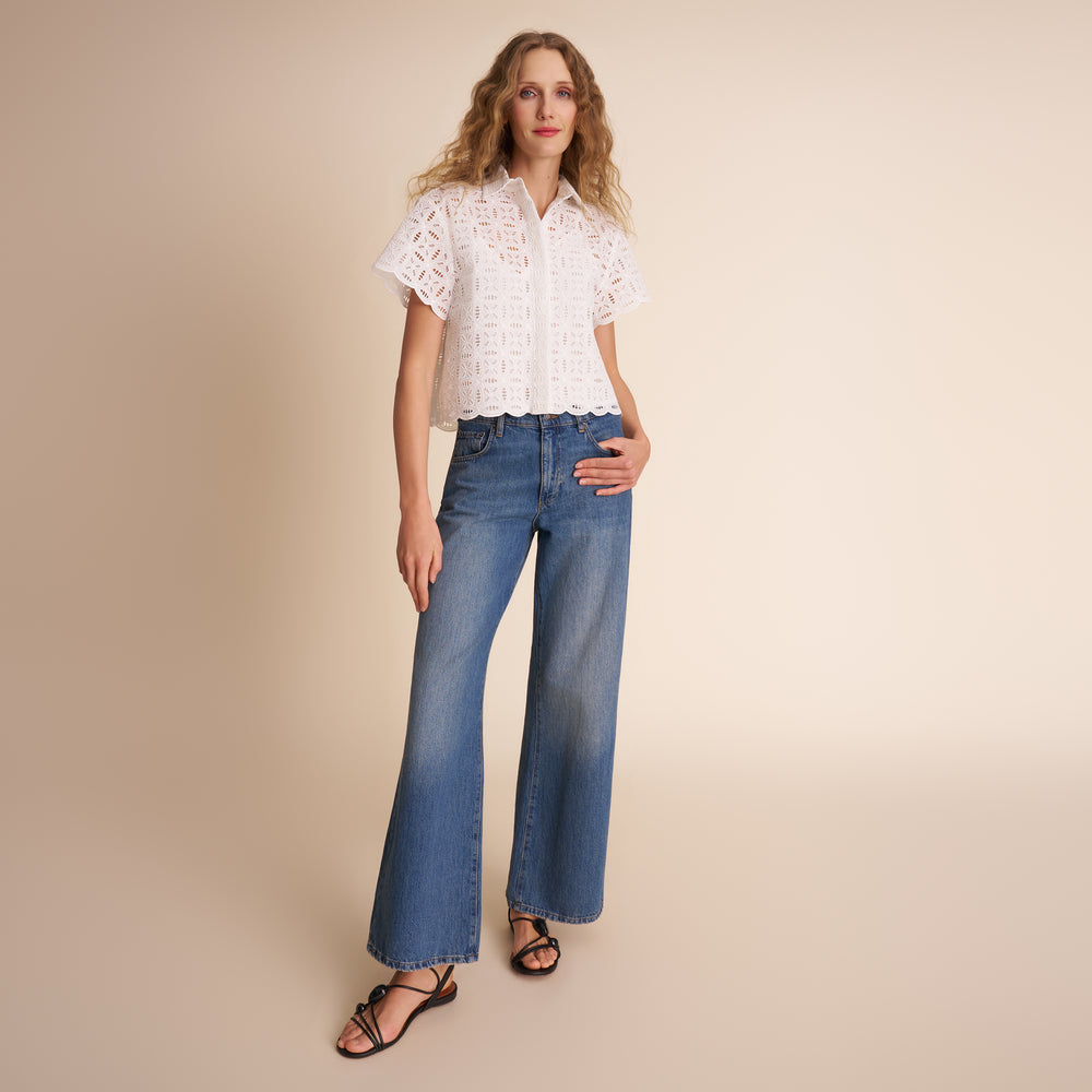 Woman wearing a white lace blouse and blue jeans on a beige background