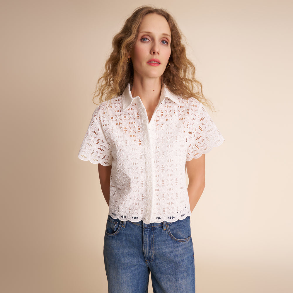 Woman wearing a white lace blouse and blue jeans against a beige background