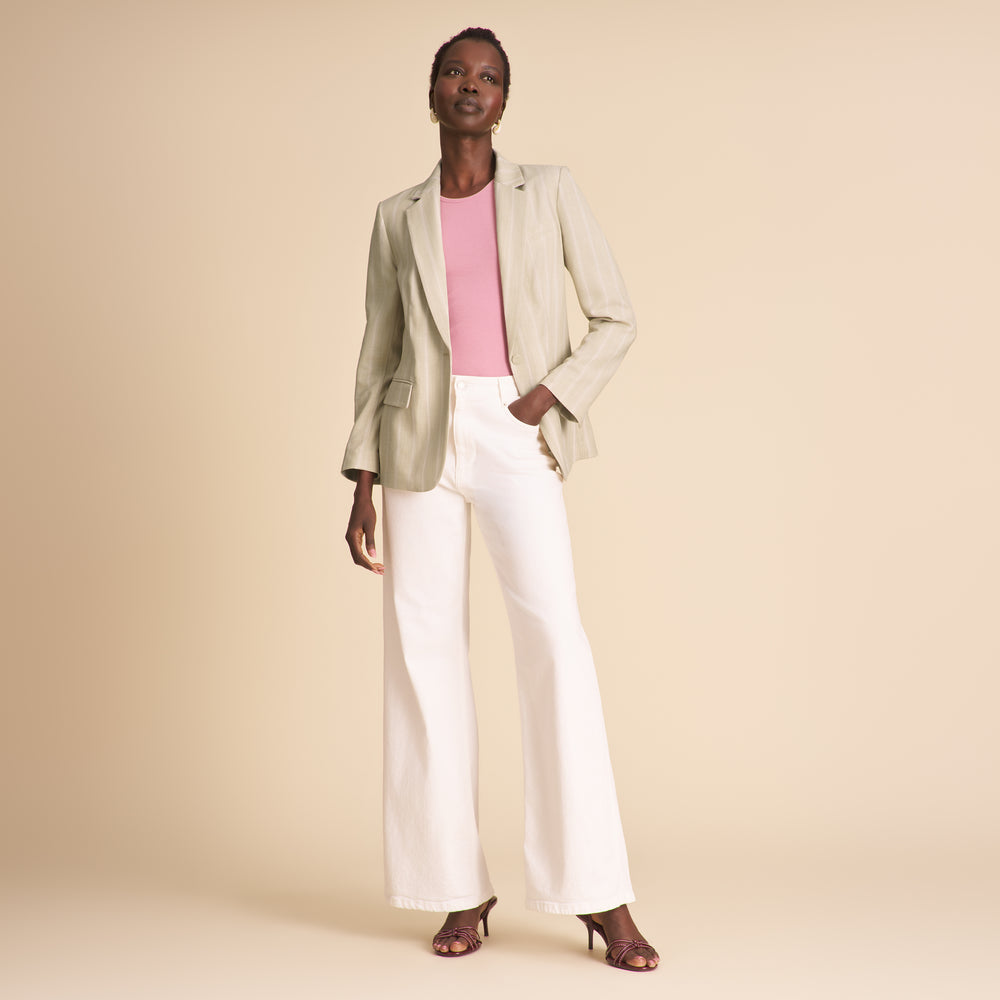 Woman wearing a light green blazer, pink top, and white pants on a beige background