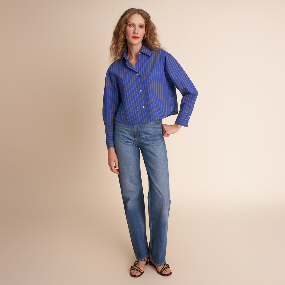 Woman wearing a blue striped shirt and jeans on a beige background