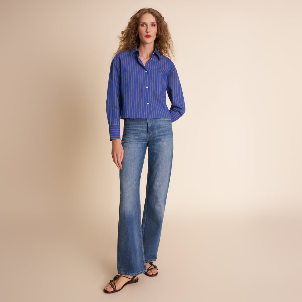 Woman wearing a blue striped shirt and jeans on a beige background