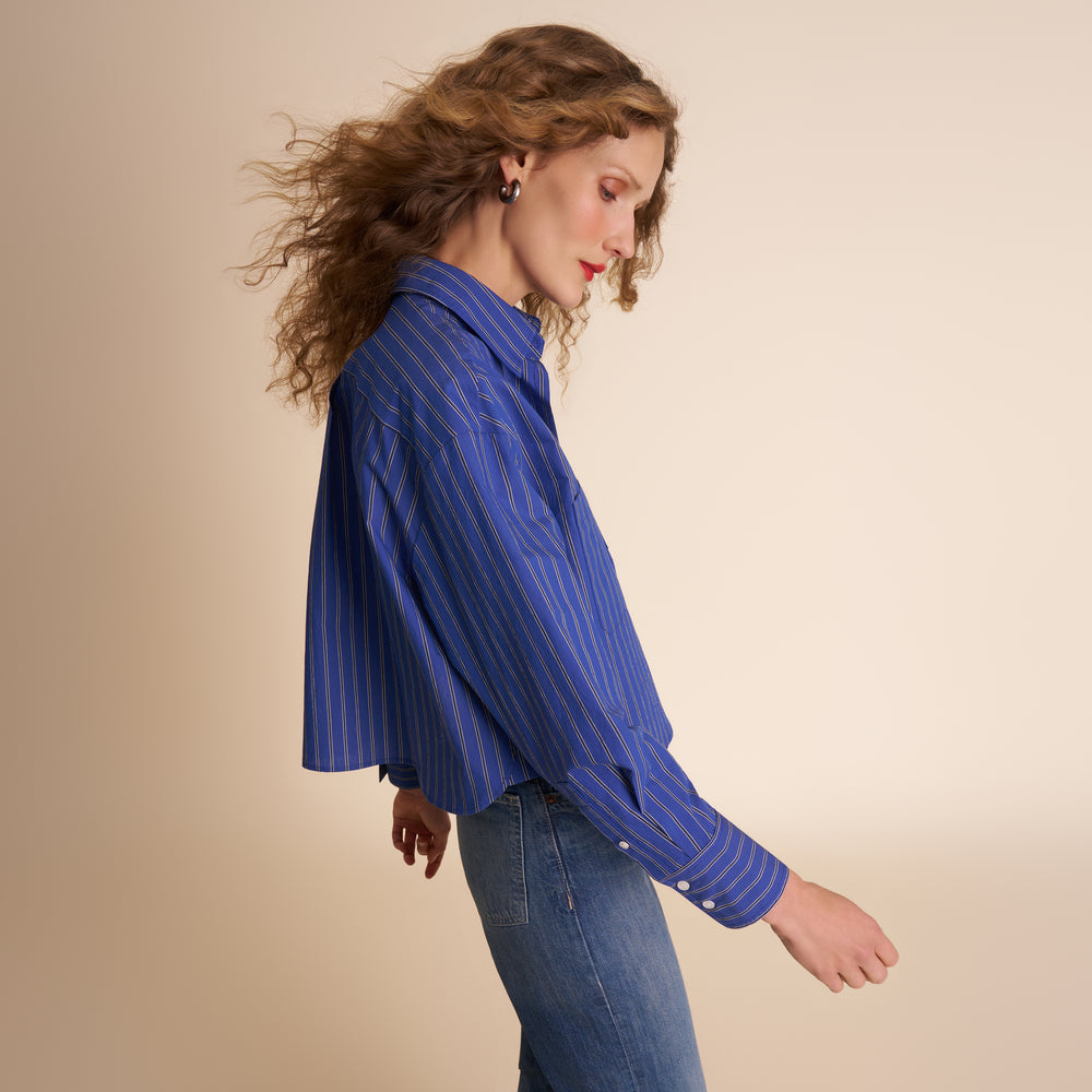 Woman wearing a blue striped shirt and jeans against a beige background