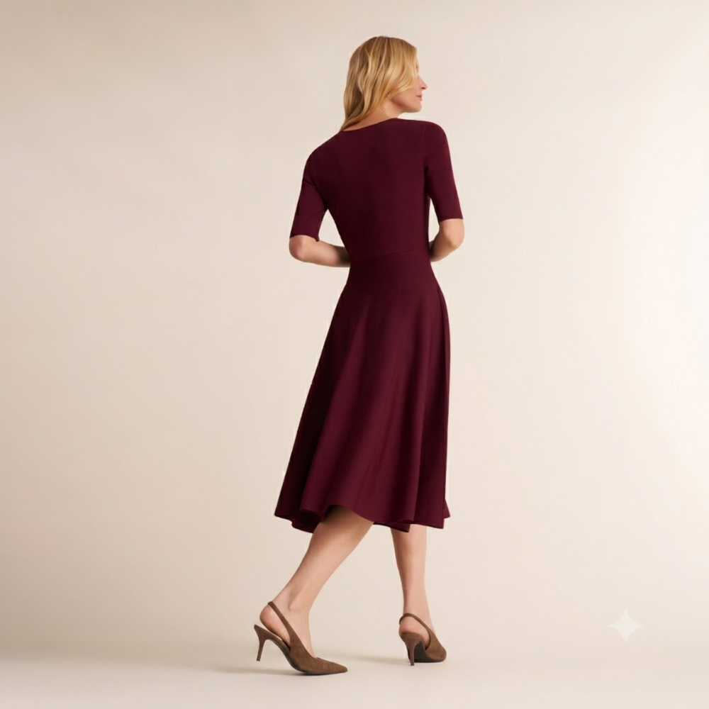 A woman wearing a short-sleeve, knee-length A-line dress in deep burgundy, shown from the back. She is wearing brown slingback heels against a plain, warm beige studio background.