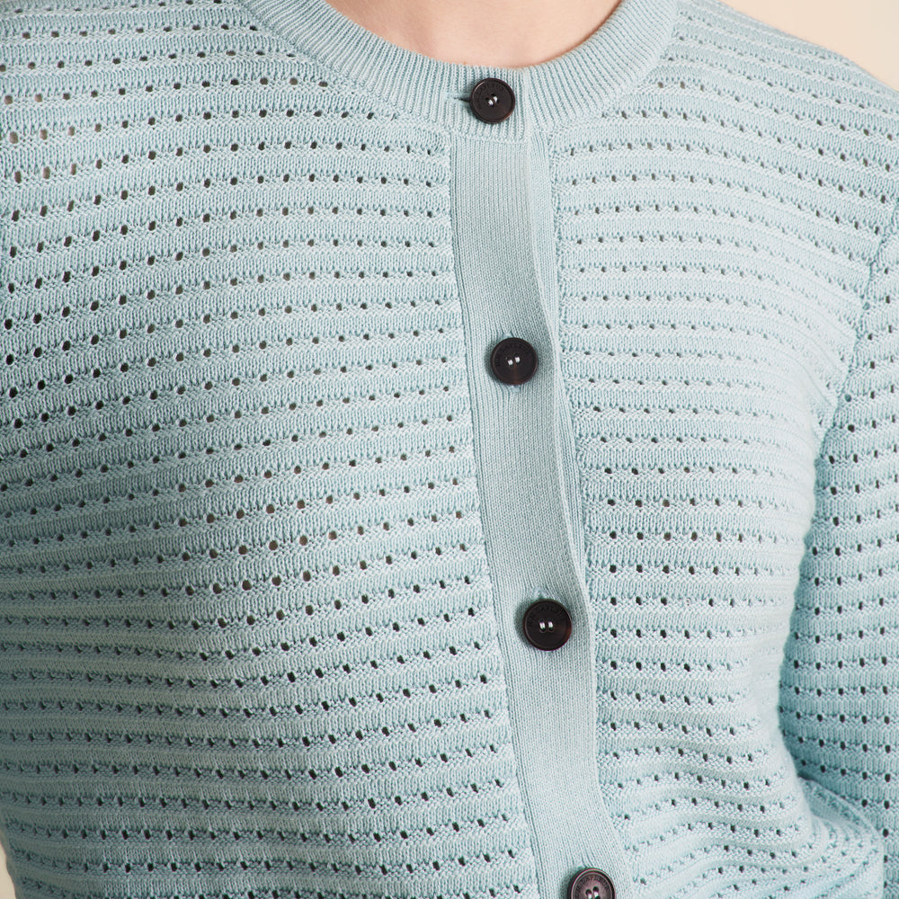 Woman wearing the Zosia cardigan in light blue on a beige background