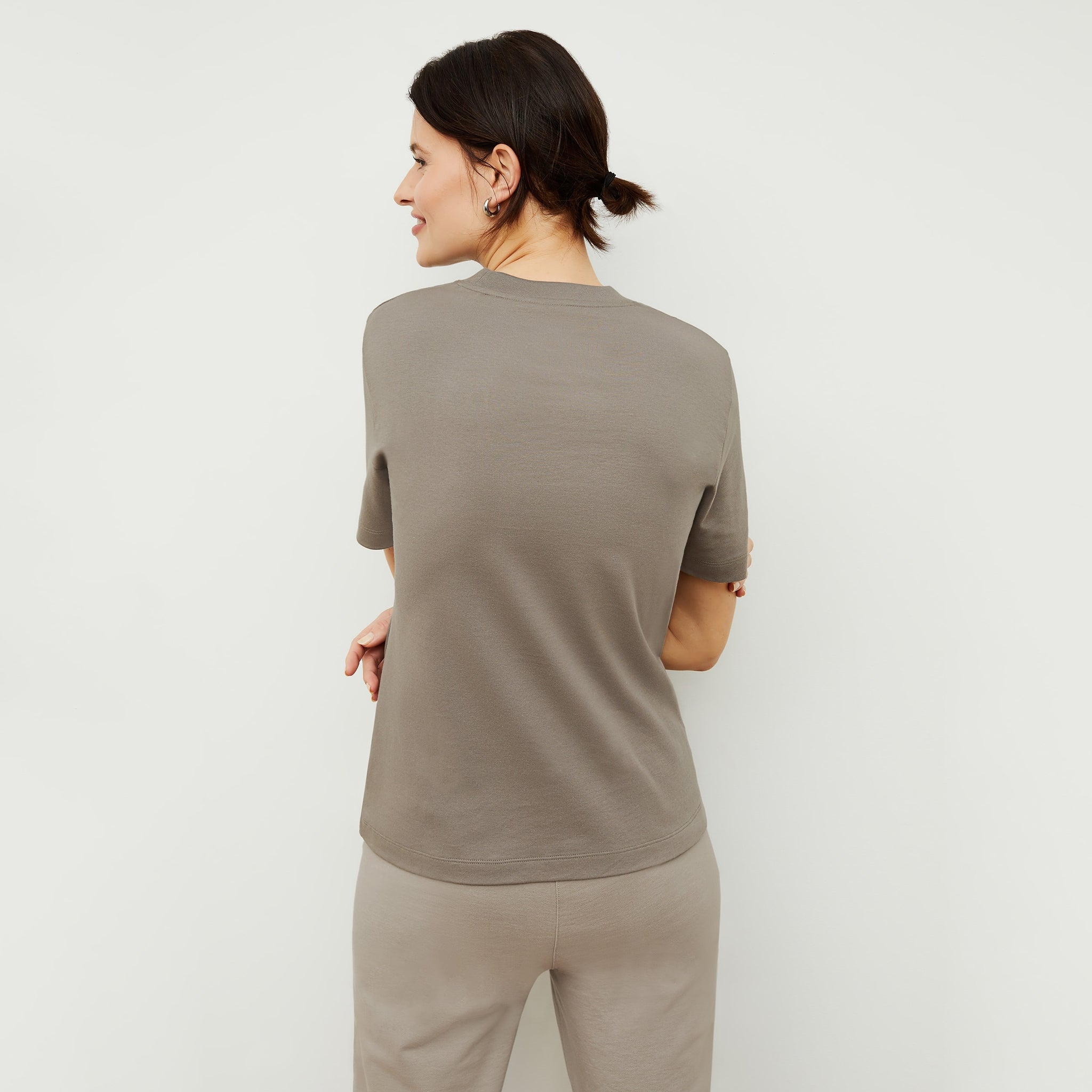 Back image of a woman standing wearing the Leslie T-Shirt—Compact Cotton in Pebble