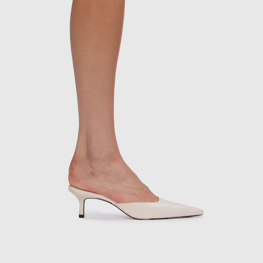 White high-heeled shoes worn with sheer tights on a light gray background