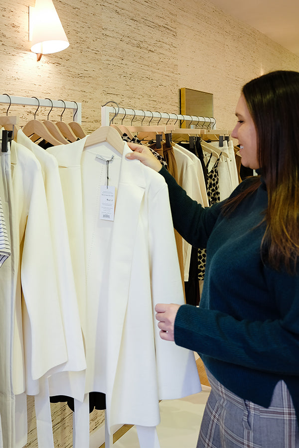 woman standing at a clothing rack holding a white jacket