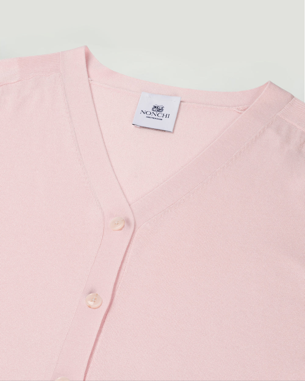 Pink cardigan with a brand label on a light gray background.