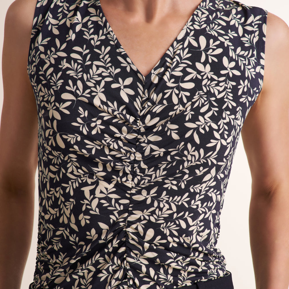 Close-up of a sleeveless V-neck top with a dark navy background and an allover cream leaf print, shown on a model.