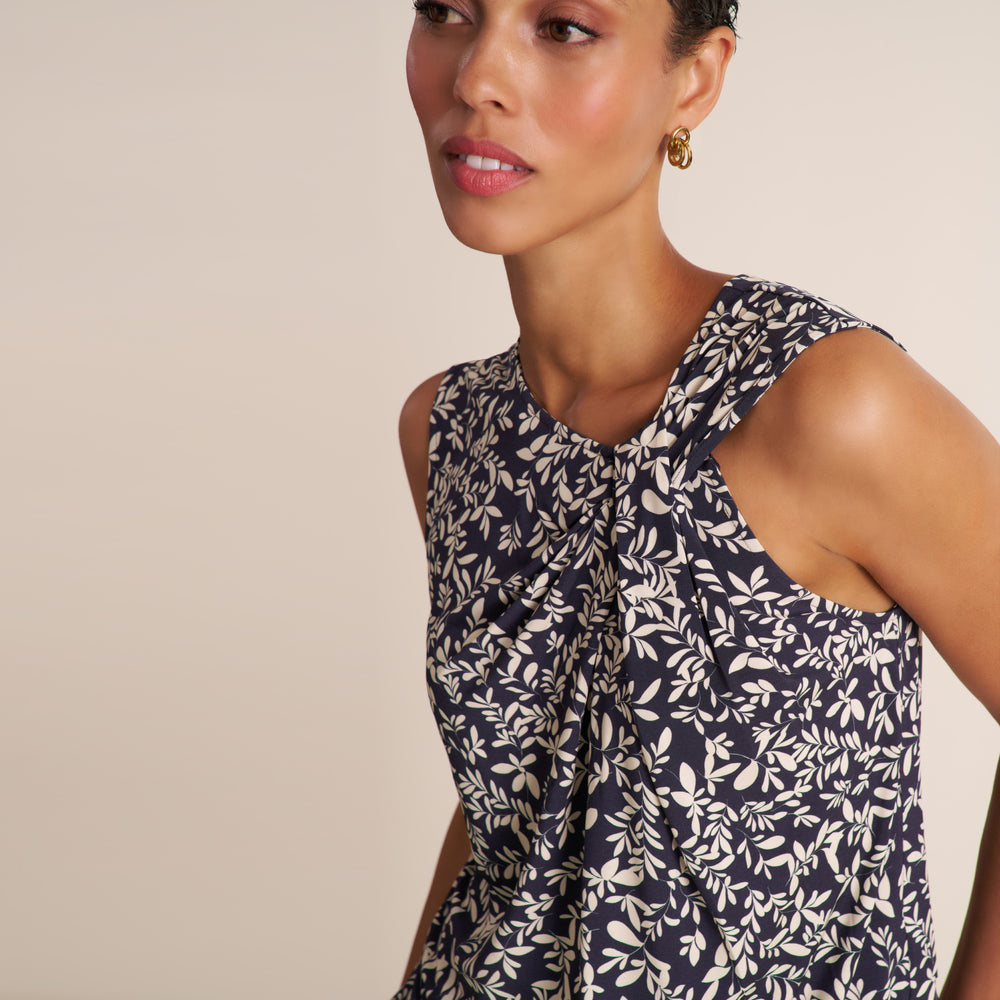 A close-up of a woman wearing a sleeveless top with a navy blue and white leafy floral pattern, set against a solid beige background.