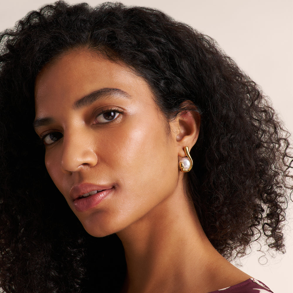 Woman wearing a aubgergine and white petal print dress and a gold and pearl earring