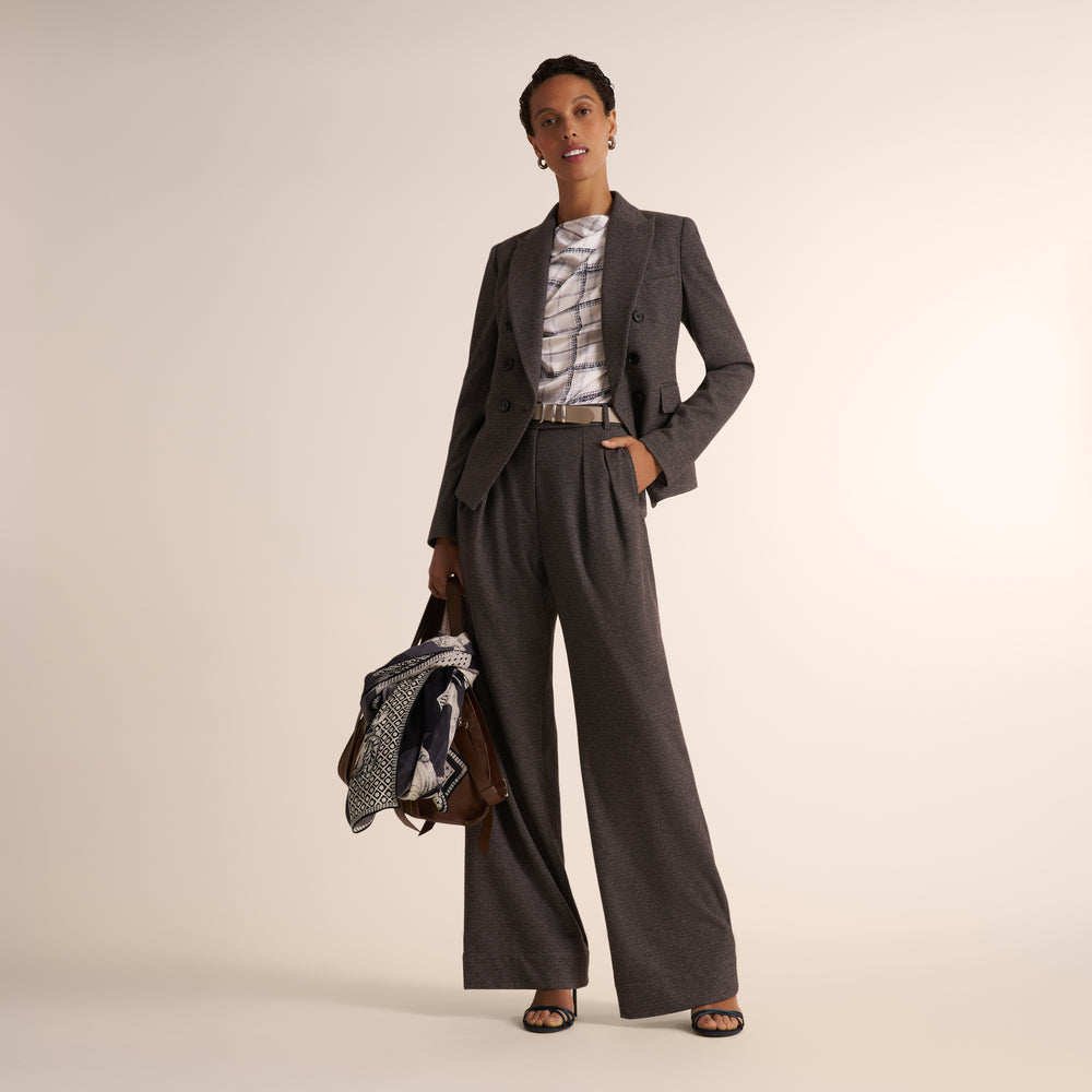 A woman modeling a white and gray plaid shirt, paired with a gray herringbone blazer and matching pants, against a plain light beige studio background.