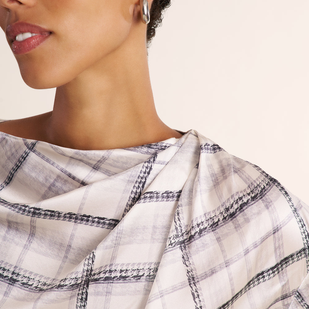 A woman modeling a white and gray plaid shirt, paired with a gray herringbone blazer and matching pants, against a plain light beige studio background.