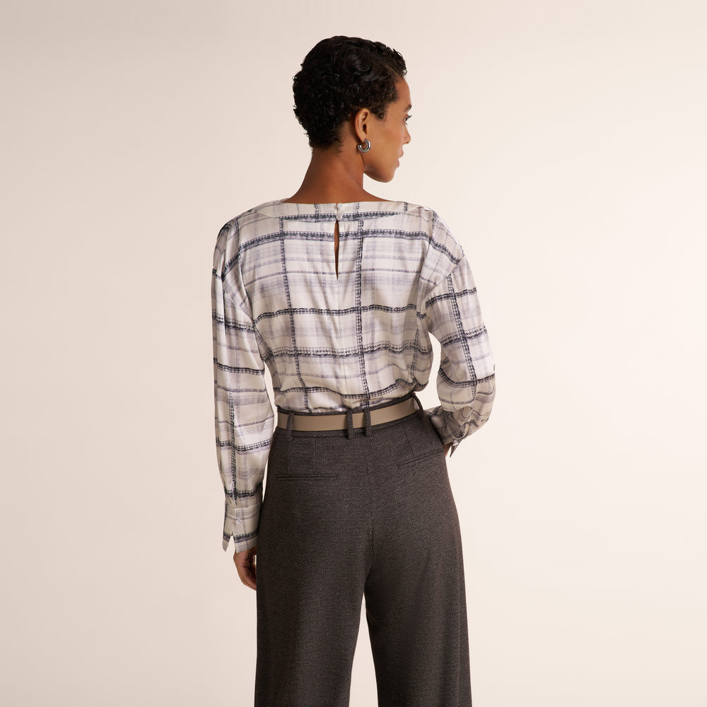 A woman modeling a white and gray plaid shirt, paired with a gray herringbone blazer and matching pants, against a plain light beige studio background.