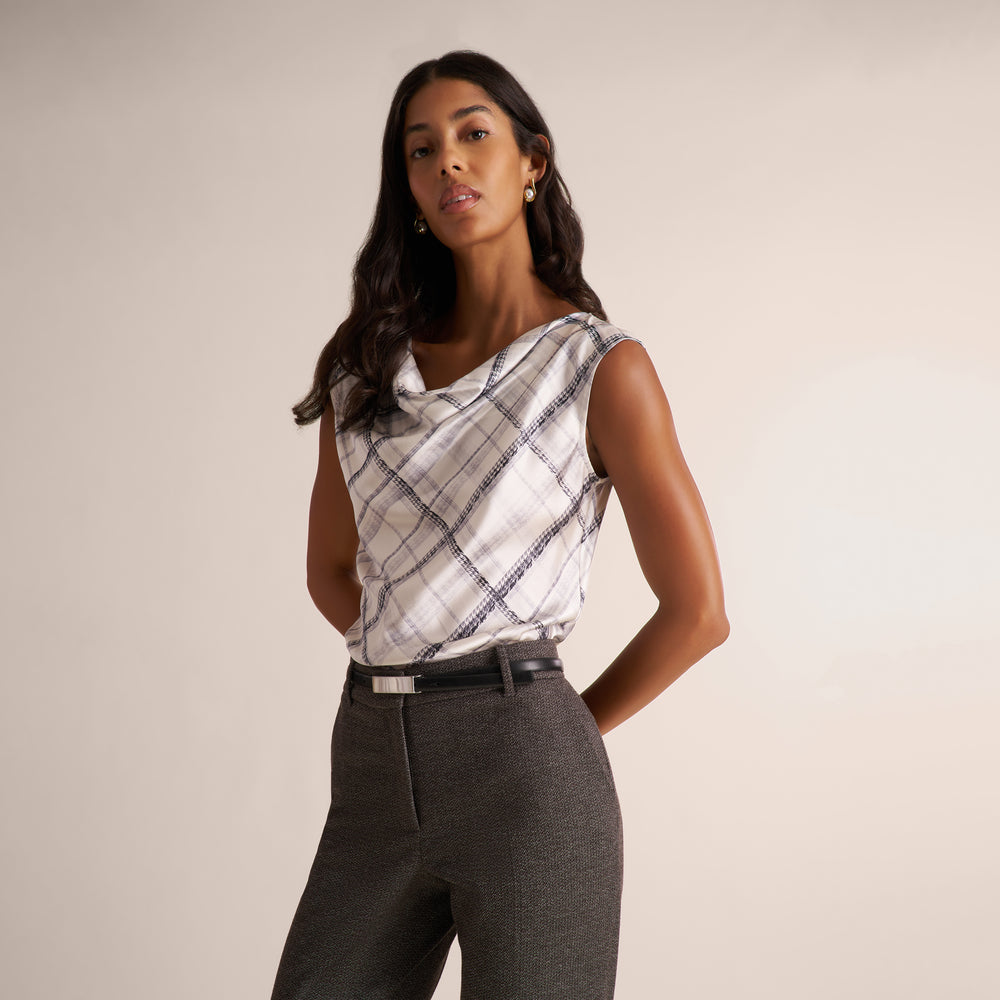 A woman modeling a white and gray plaid shirt, paired with a gray herringbone blazer and matching pants, against a plain light beige studio background.