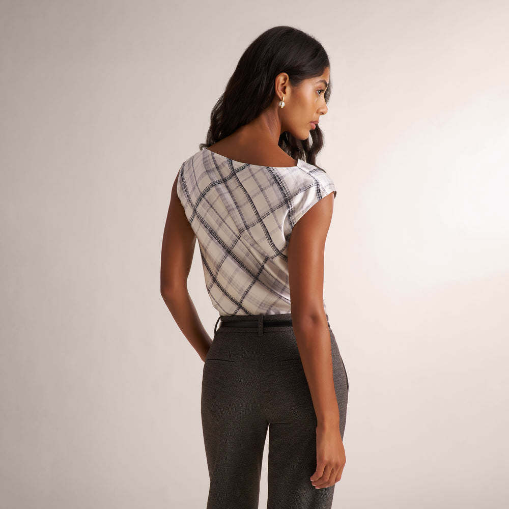 A woman modeling a white and gray plaid shirt, paired with a gray herringbone blazer and matching pants, against a plain light beige studio background.