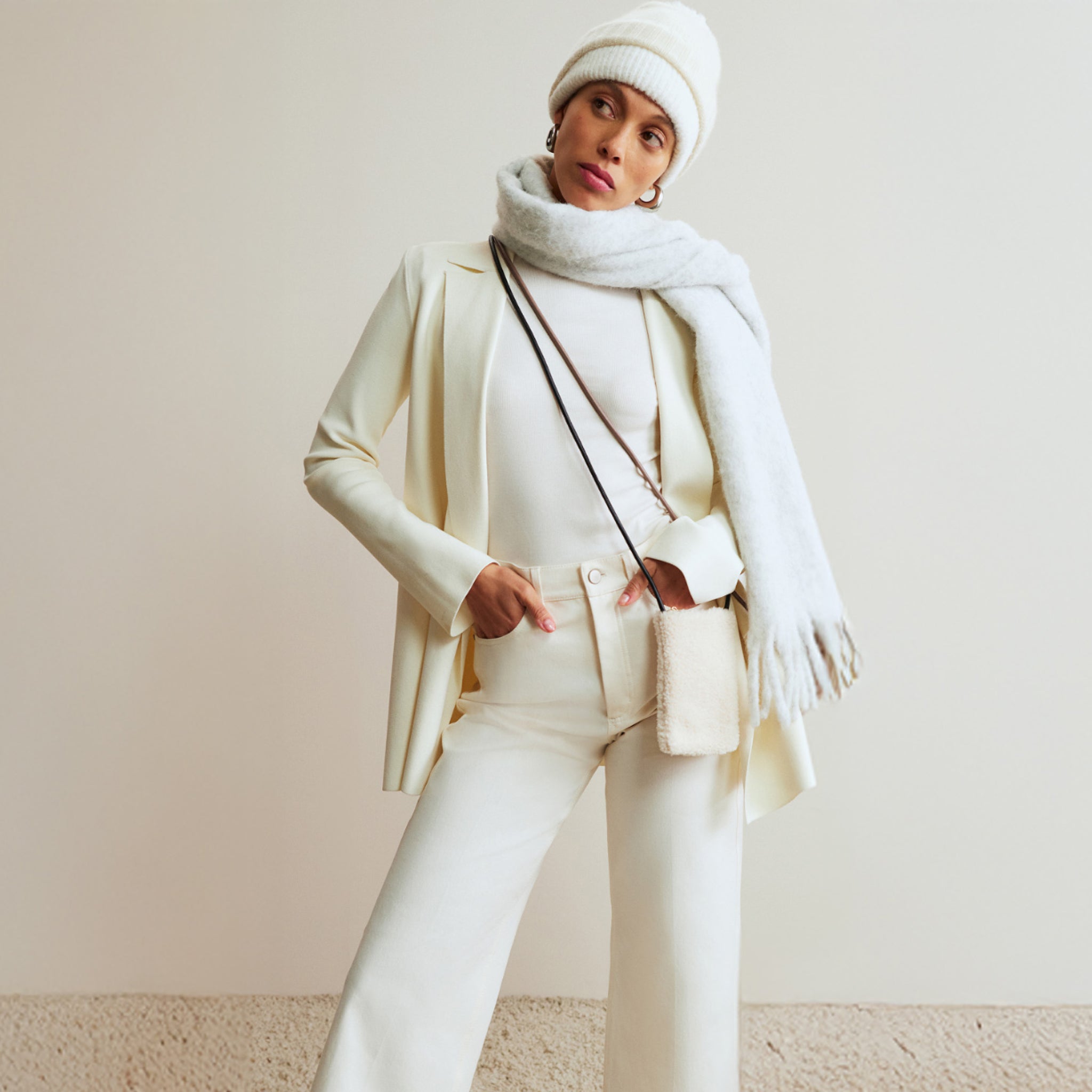Person wearing a white outfit with a coat, pants, scarf, and beanie against a plain background