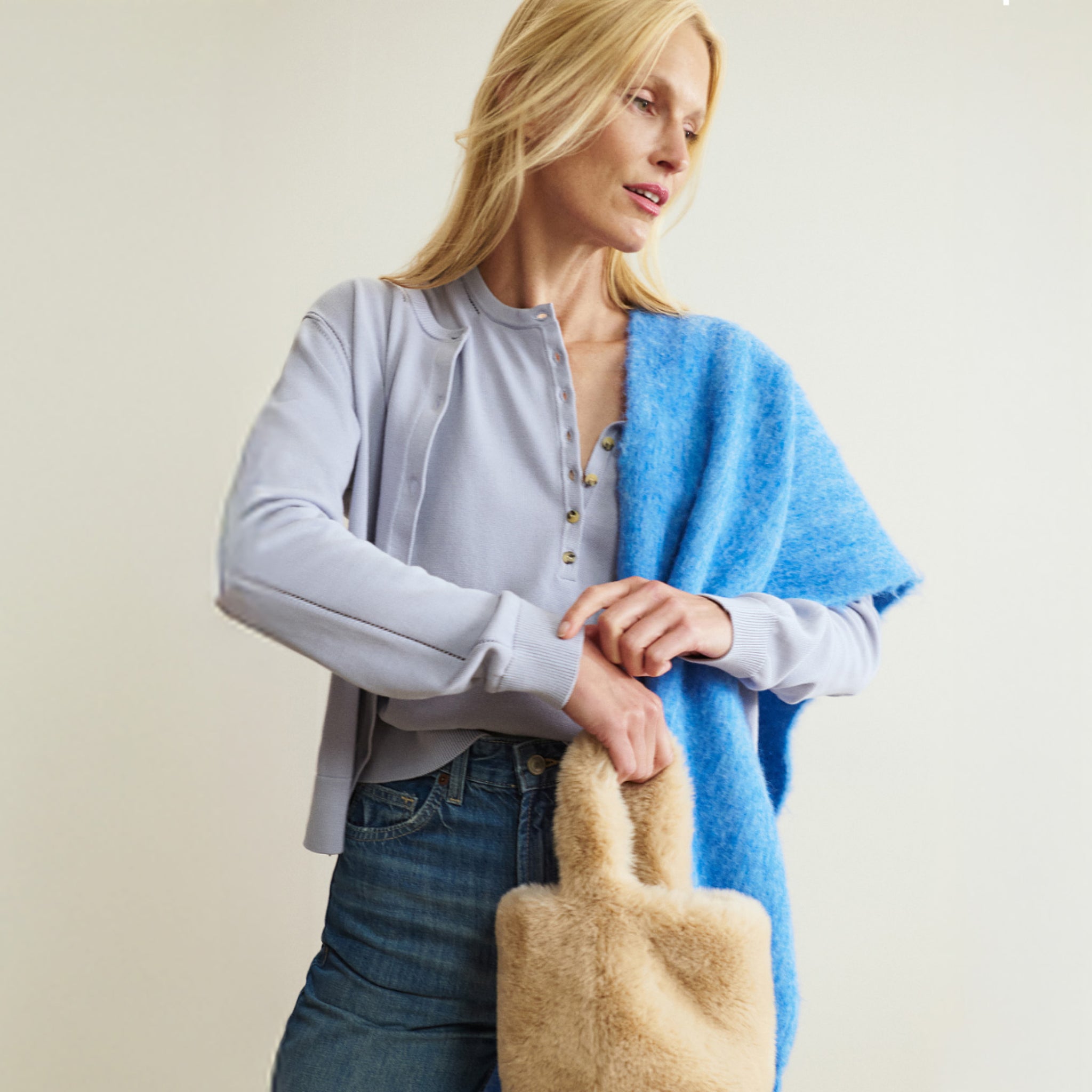 Woman holding a beige handbag against a plain background