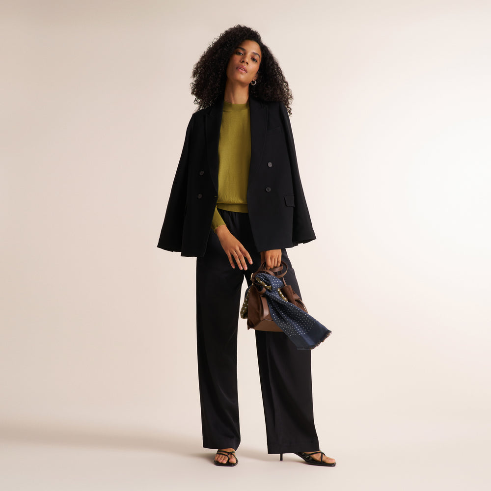 Woman wearing an olive green color long sleeve sweater with black blazer and wide leg pants