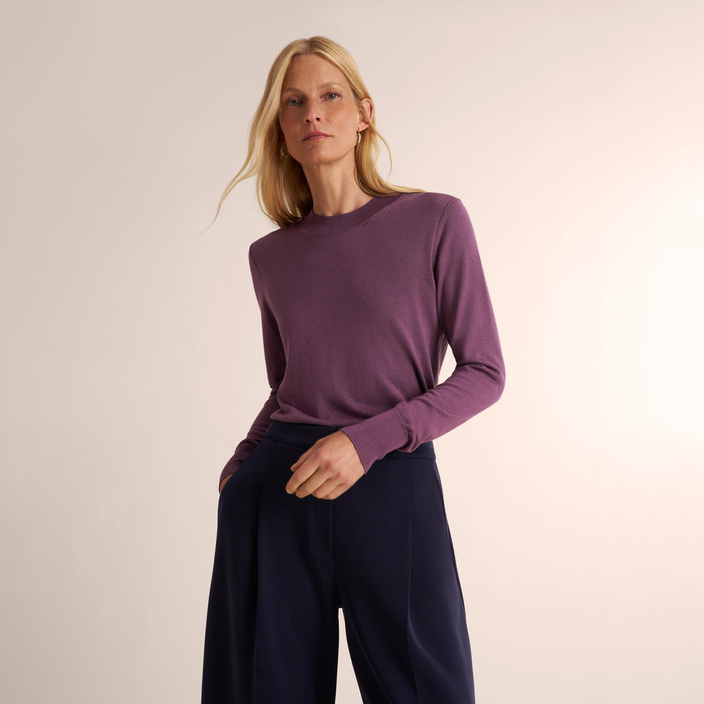 Woman wearing a purple fig color long sleeve sweater with navy wide leg pants
