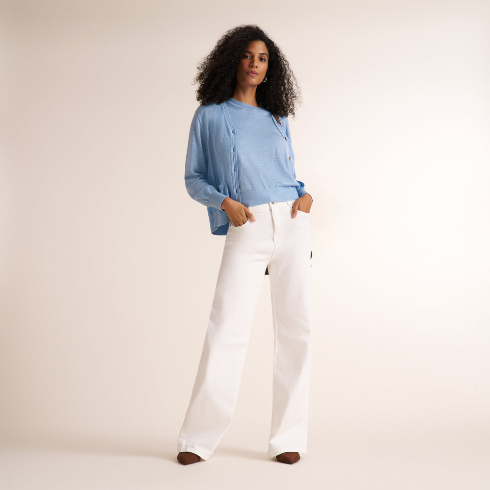 Woman wearing alight blue short sleeve sweater tank with a matching cardigan and wide leg white jeans