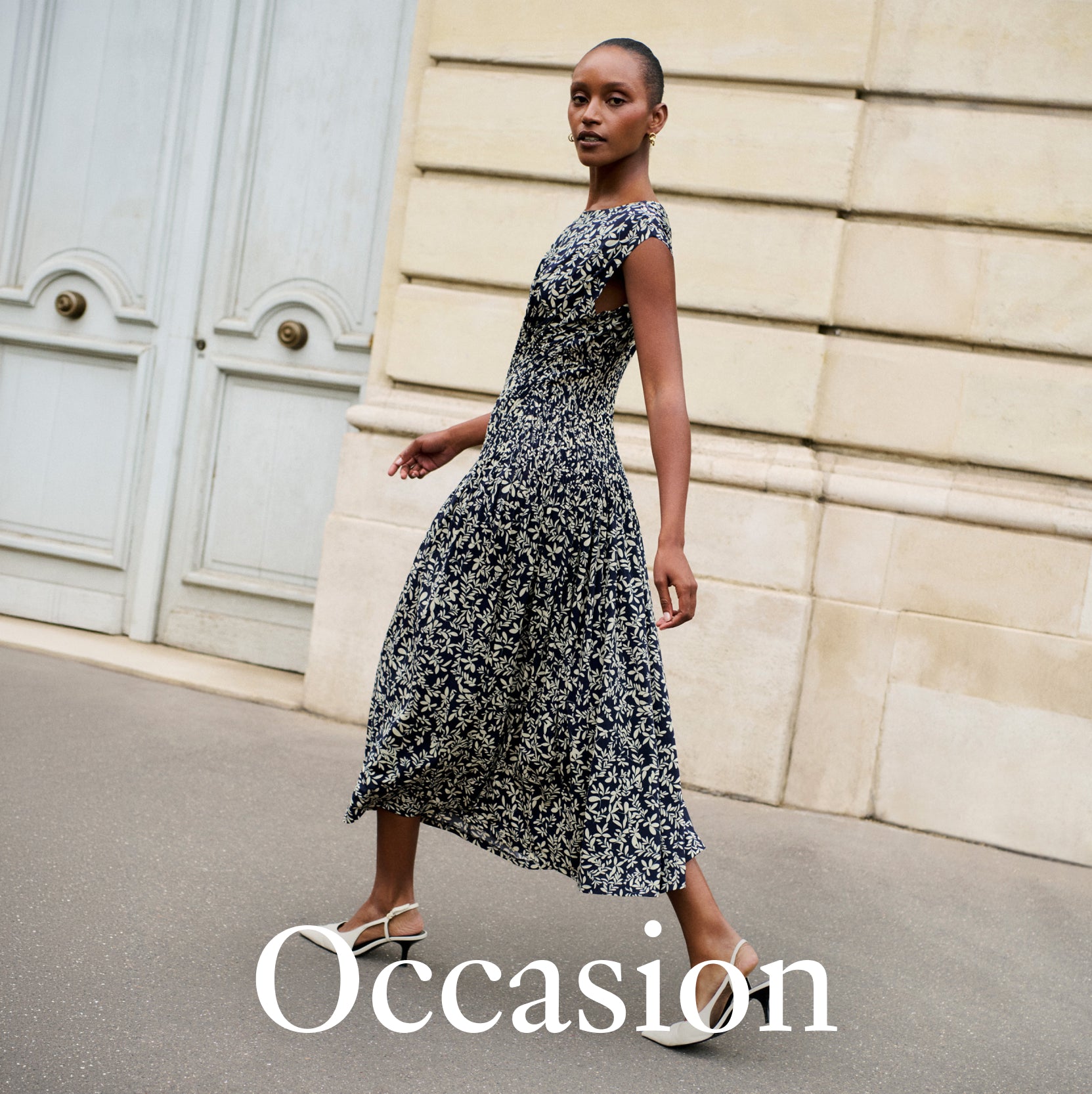 A woman wearing a sleeveless black and white floral midi dress walks outdoors in front of a beige stone wall and pale blue doors. The word 'Occasion' is overlaid at the bottom.