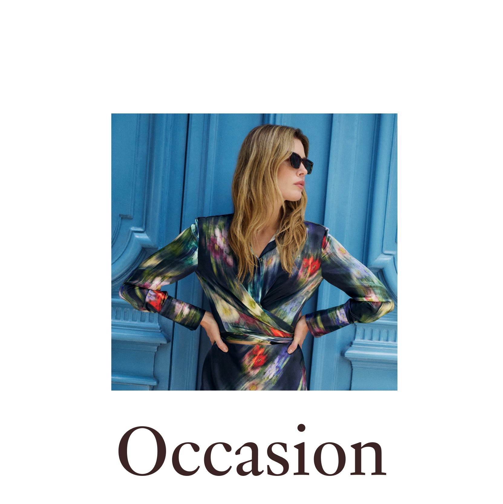 A woman wearing a long-sleeve wrap dress with a colorful abstract print in green, blue, red, and black, posed in front of a blue paneled wall. The word 'Occasion' is printed below the photo.