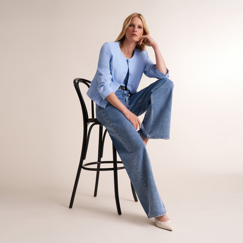 Woman sitting on a chair wearing the Aniya jacket in light blue with jeans