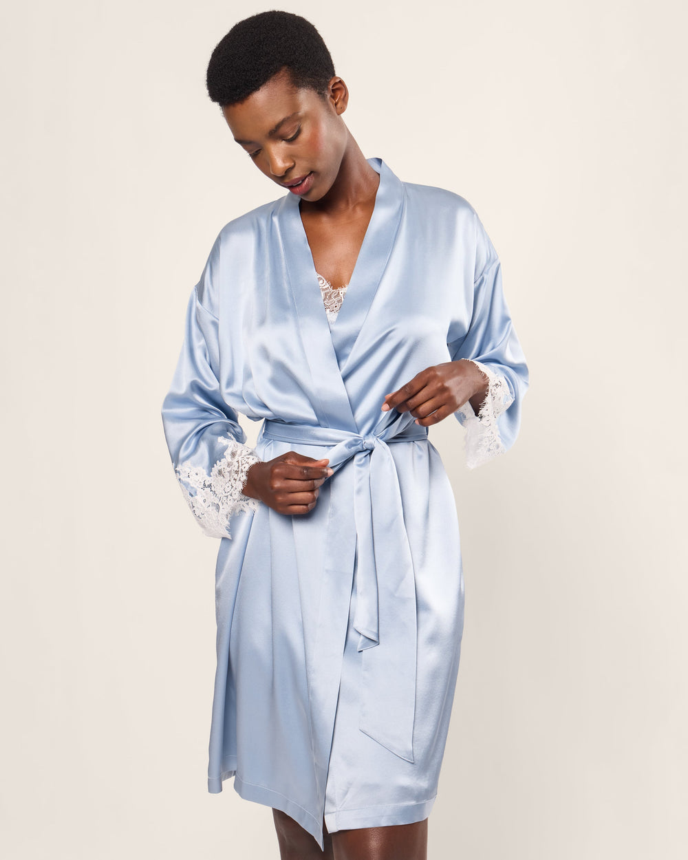 Woman wearing a light blue satin robe with lace trim on a plain background