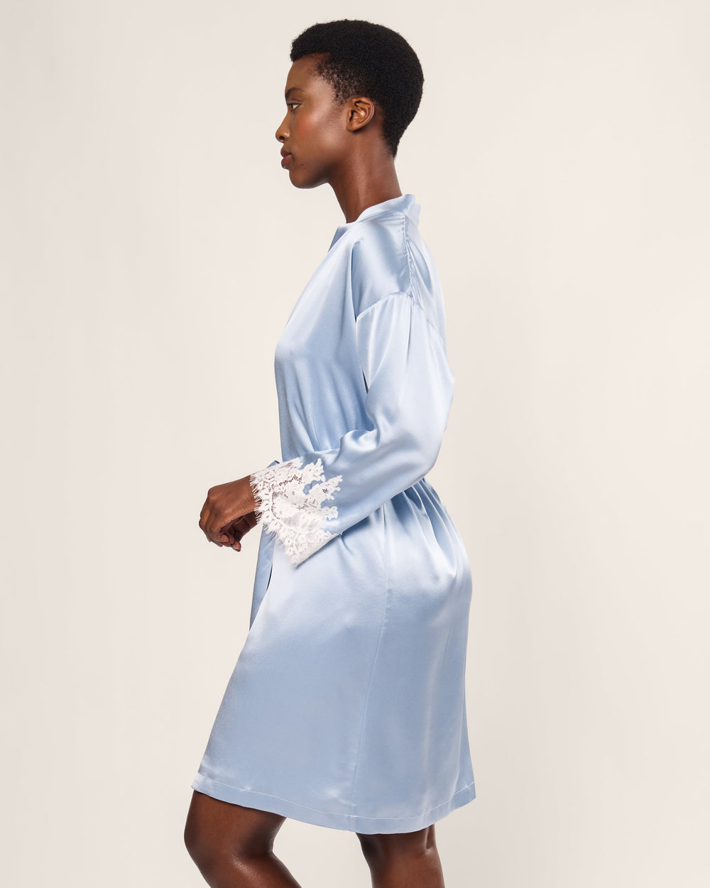 Woman wearing a light blue satin robe with lace cuffs on a beige background