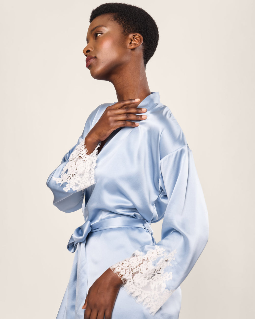 Woman wearing a light blue satin robe with lace cuffs and hem on a plain background