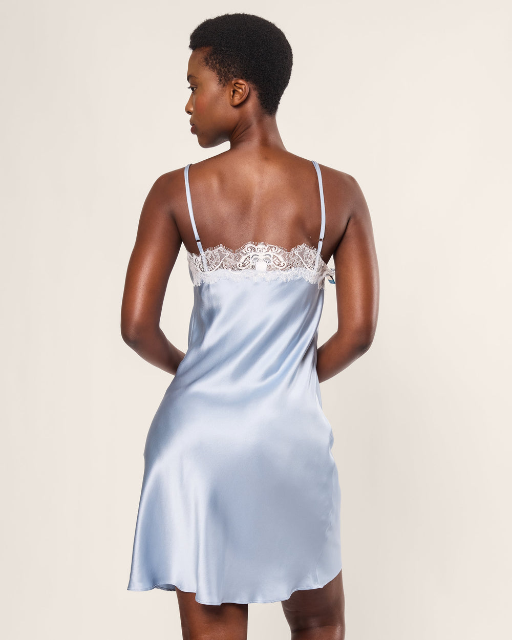Woman wearing a light blue satin nightgown with lace trim on a plain background
