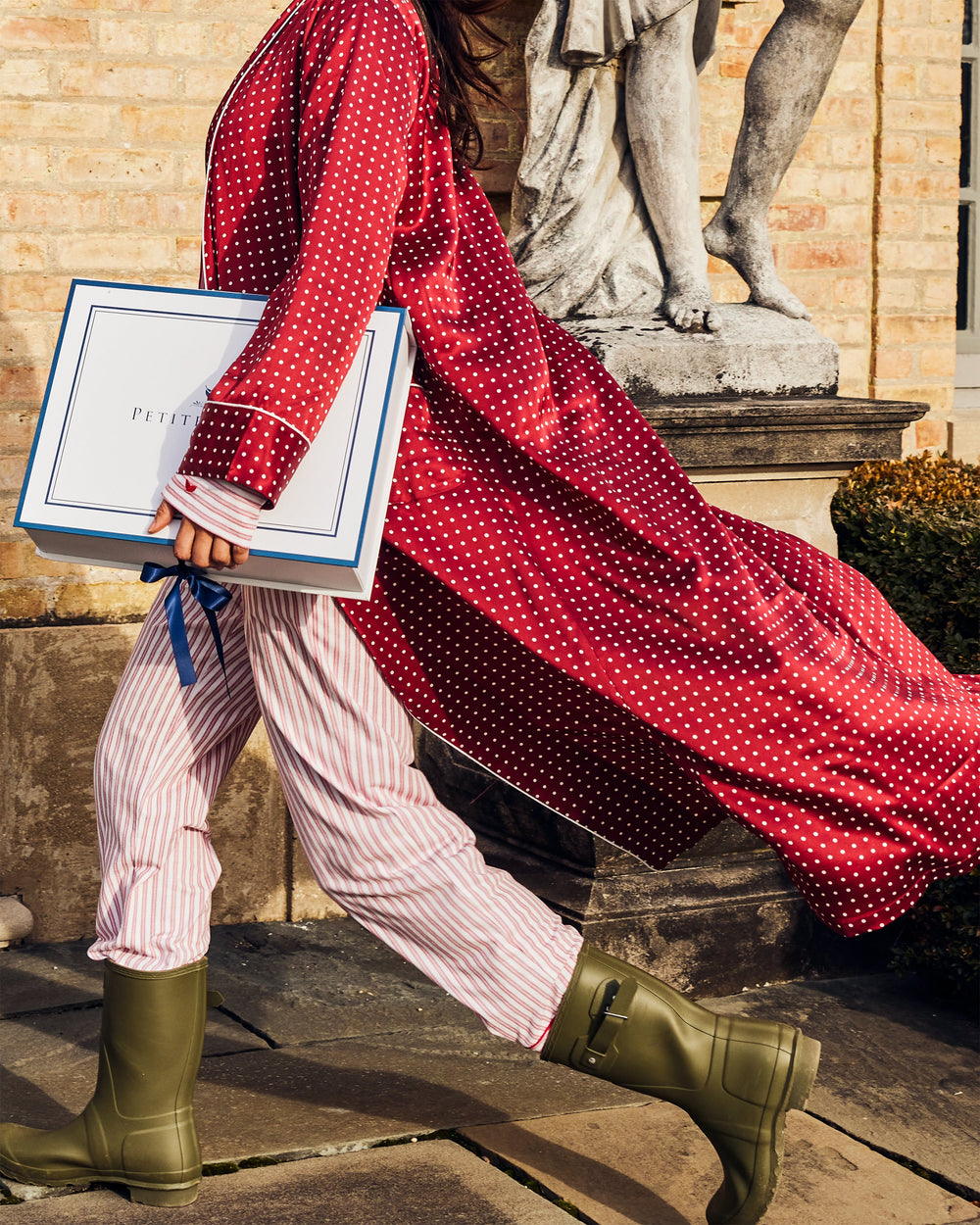 Person in red polka dot coat and green wellies holding books in a classical setting