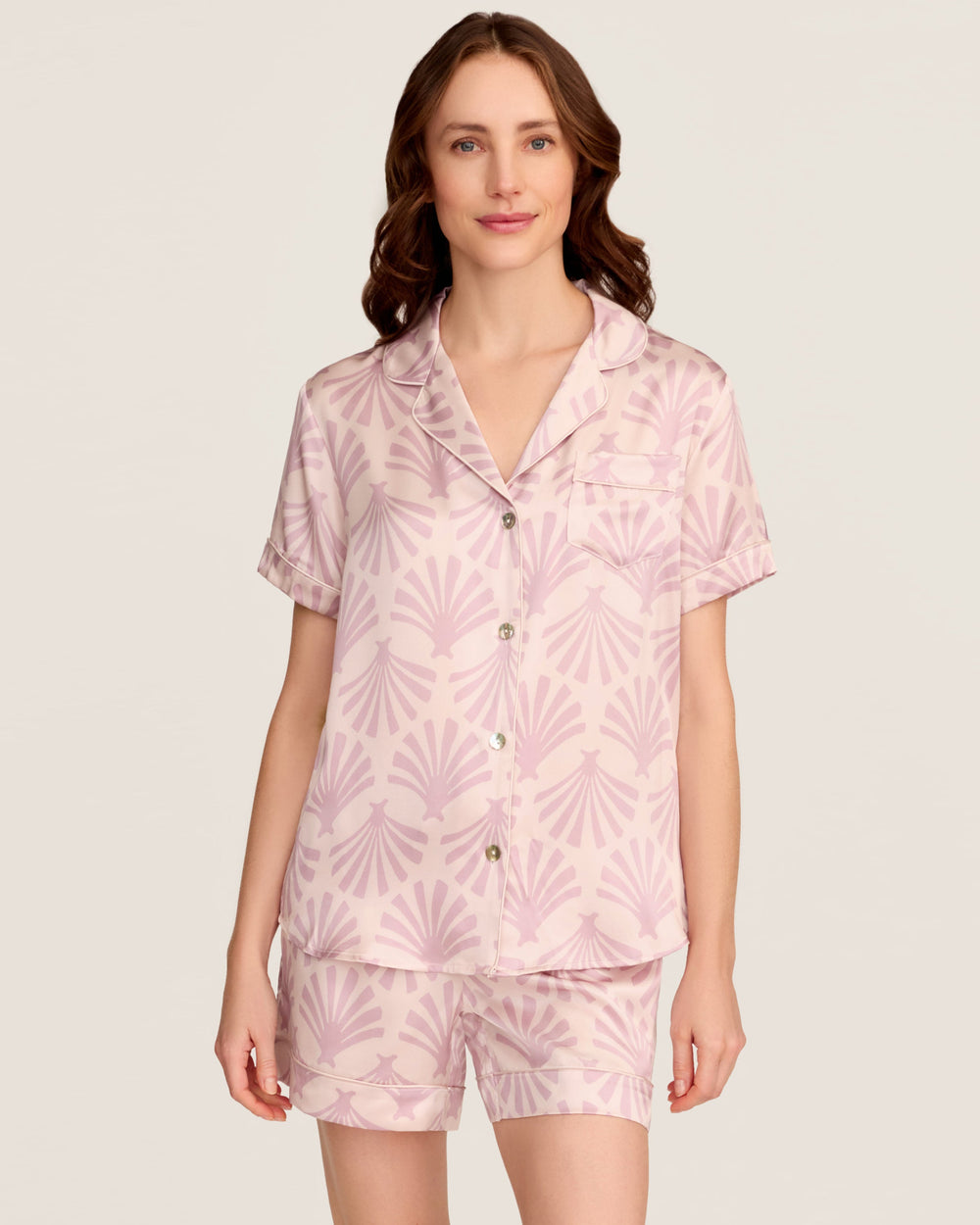 Woman wearing a pink pajama set with a leaf pattern on a plain background