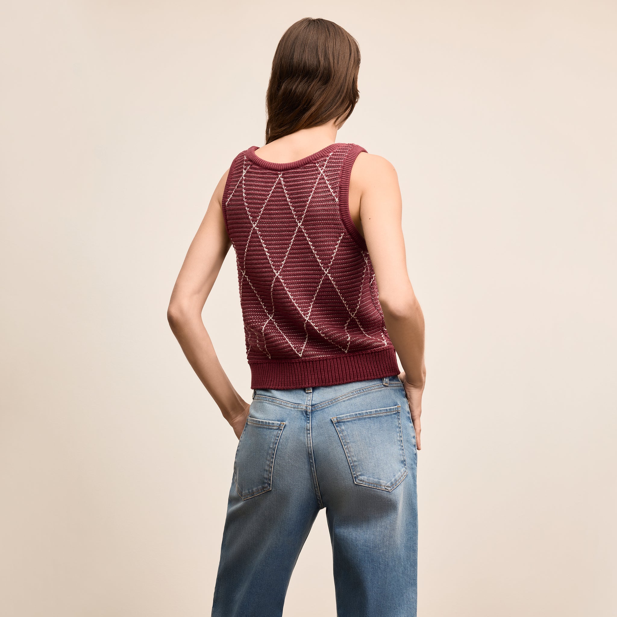 Woman wearing a maroon knitted tank top and blue jeans on a beige background
