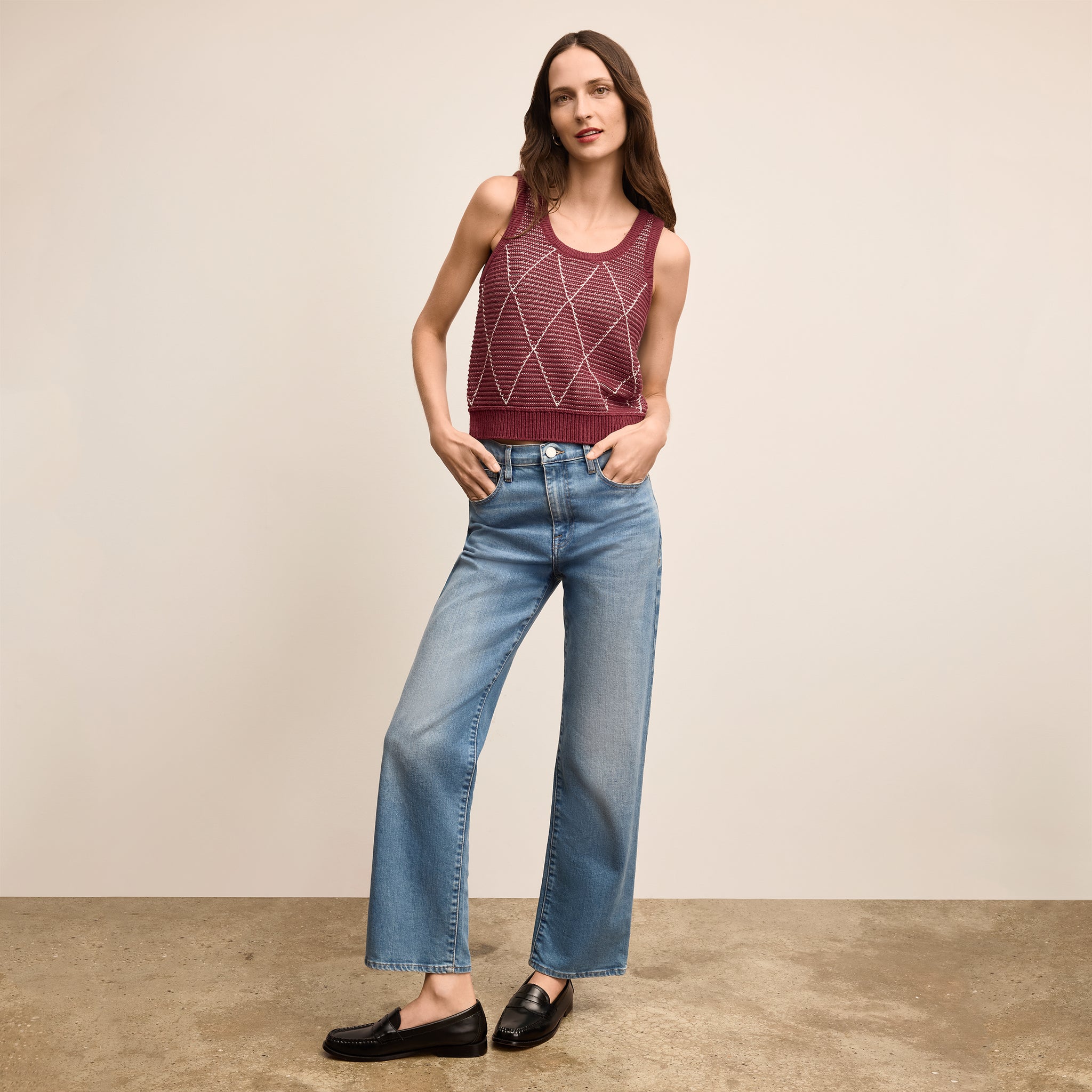 Woman wearing a red tank top and blue jeans against a beige background